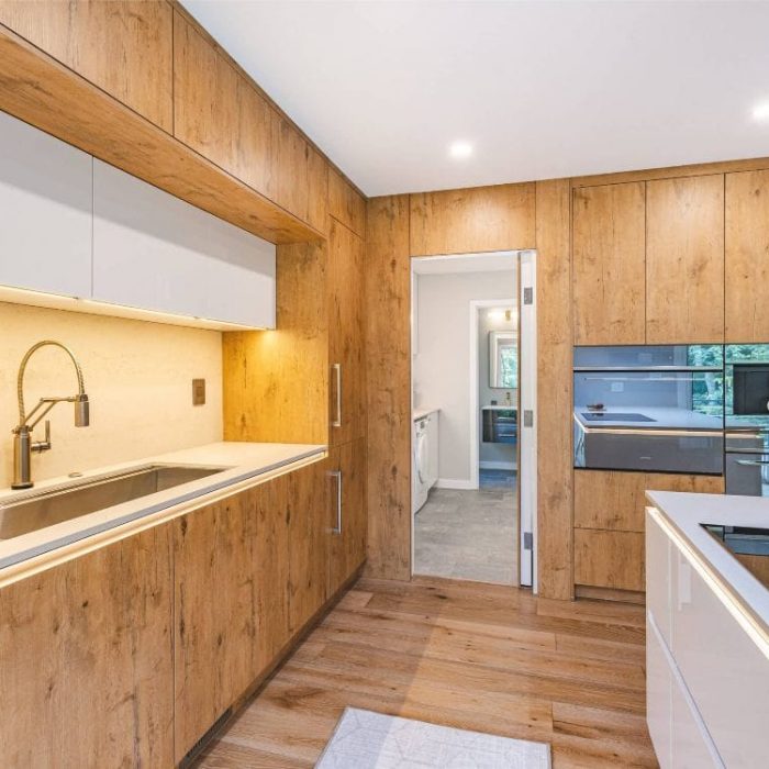 Modern kitchen featuring integrated Miele appliances, natural wood-grain cabinetry, and a white island with LED lighting.